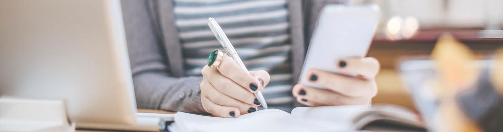 woman writing while looking at her mobile device