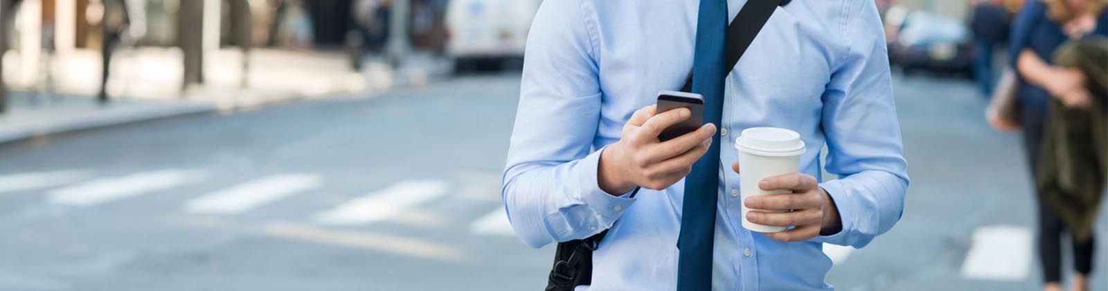 business man walking in the city while holding coffee and looking at mobile device