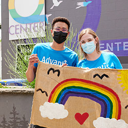 Two Advantis team members posing together during a LGBTQ+ Pride volunteer event. They are holding up a painted sign of a rainbow and heart.
