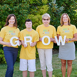 Four smiling team members from the Wheel to Walk Foundation, wearing yellow t-shirts with the Wheel to Walk logo and each holding a large white letter to spell out G-R-O-W.