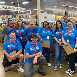 Ten Advantis employee volunteers gathered together for a group photo inside the Beaverton Fred Meyer's. Most are wearing blue shirts with the Advantis logo, and everyone is smiling.